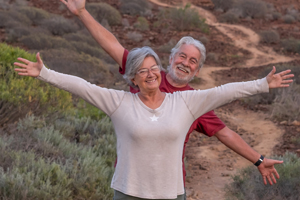 older couple grinning with out stretched arms on a hiking trail