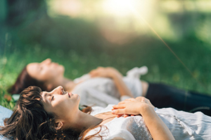 Two women laying on their backs in the grass with eyes closed