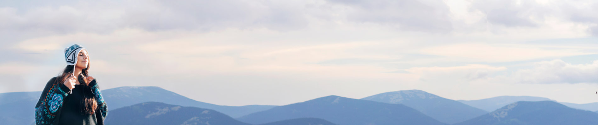 A woman in a stocking cap and wrap with mountains in the background