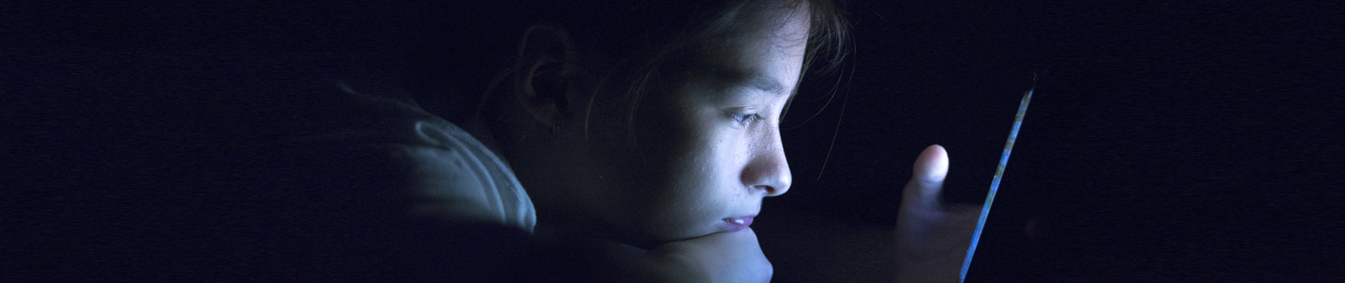 an adolescent looking at a computer screen in a dark room