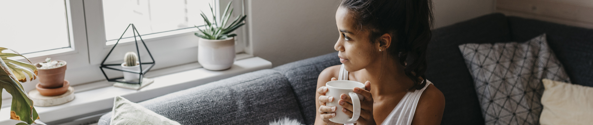 Woman gazing out window on couch with coffee
