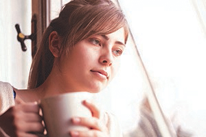 Woman holding a mug, resting her head on a window while gazing through it